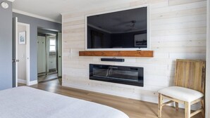 Uma sala de estar moderna com uma televisão de tela plana grande fixada acima de uma lareira, piso de madeira e design minimalista.