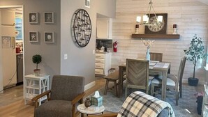 Uma sala de estar moderna com uma mesa de jantar de madeira, duas poltronas, uma mesa de centro e uma lareira com um relógio.