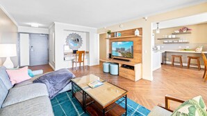 A modern living room with a sofa, coffee table, TV, and a kitchen area with stools and shelves. - Oceanfront Condo W Free Valet Parking & Balcony (Honolulu)