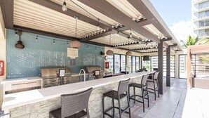 An outdoor bar area with a stone counter, bar stools, and a grill. - Oceanfront Condo W Free Valet Parking & Balcony (Honolulu)