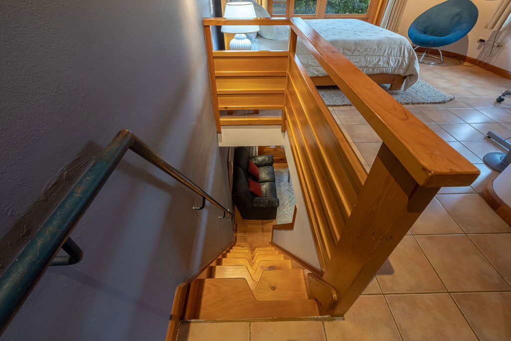 Una escala de fusta que condueix a una habitació amb un llit, una cadira i una finestra.