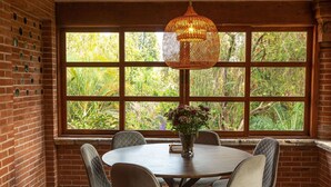 Uma área de refeições com uma mesa redonda, quatro cadeiras, um lustre e uma janela grande com vista para o verde.