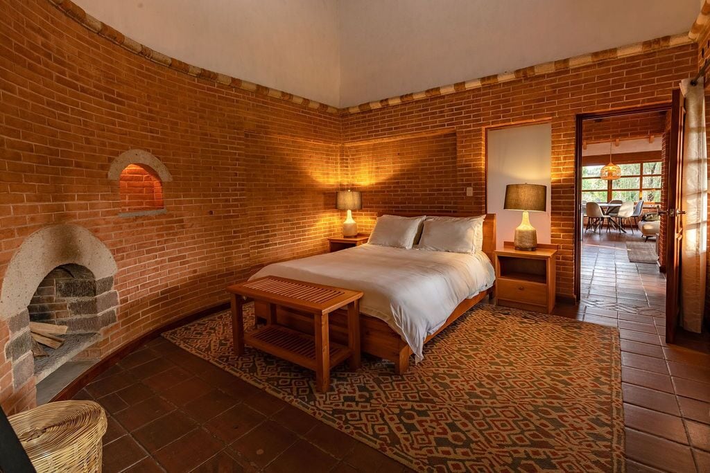 A cozy room with a brick wall, a bed, a small table, and a fireplace.