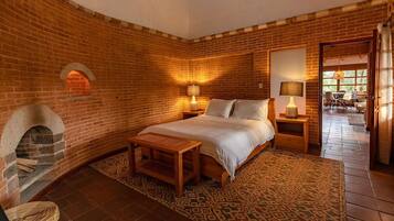 A cozy room with a brick wall, a bed, a small table, and a fireplace.