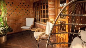 Uma área de estar ao ar livre aconchegante, com cadeiras de vime e uma cadeira suspensa, cercada por paredes de tijolo e plantas em vasos.