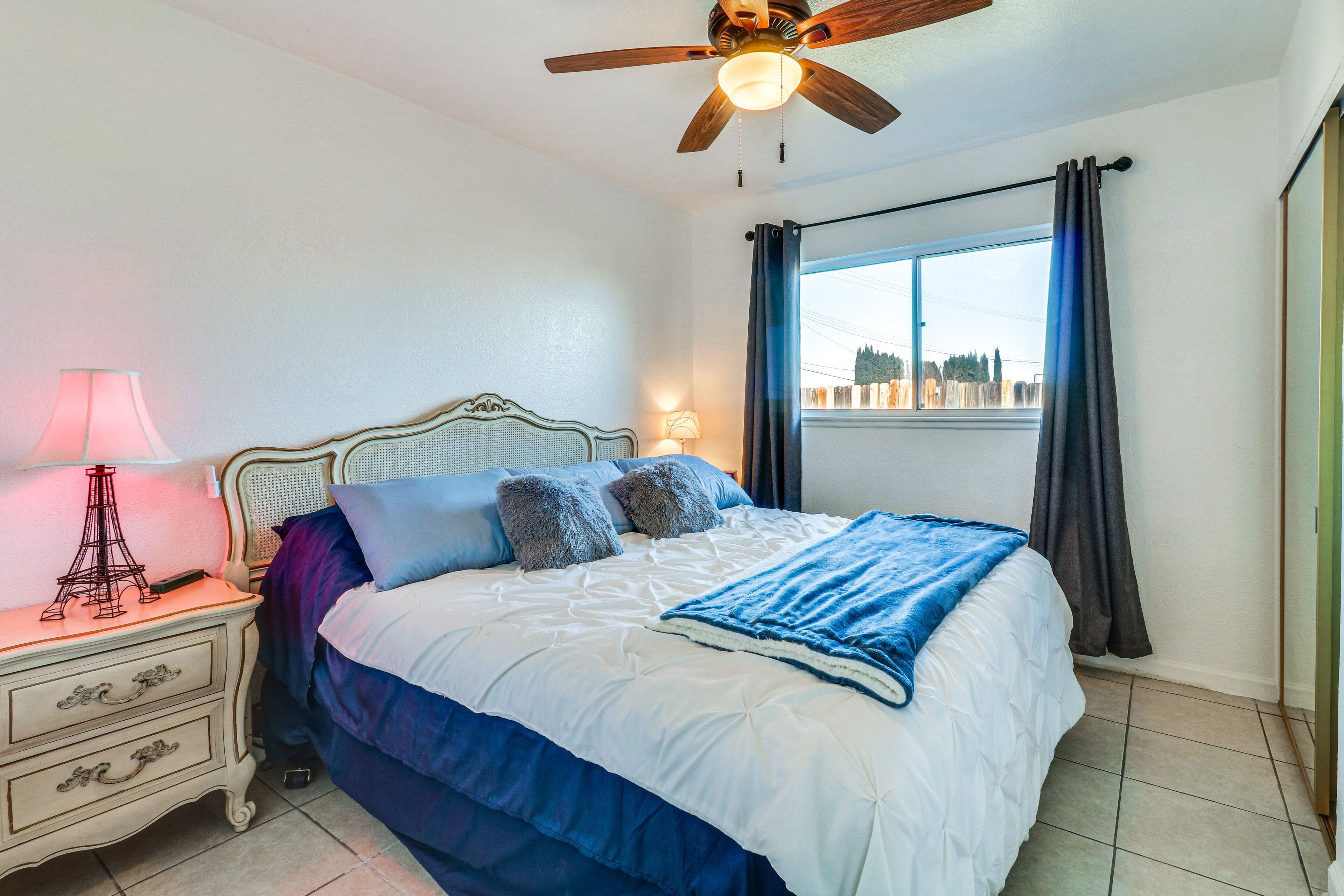A bedroom with a bed, bedside lamps, a nightstand, a ceiling fan, and a window with curtains.