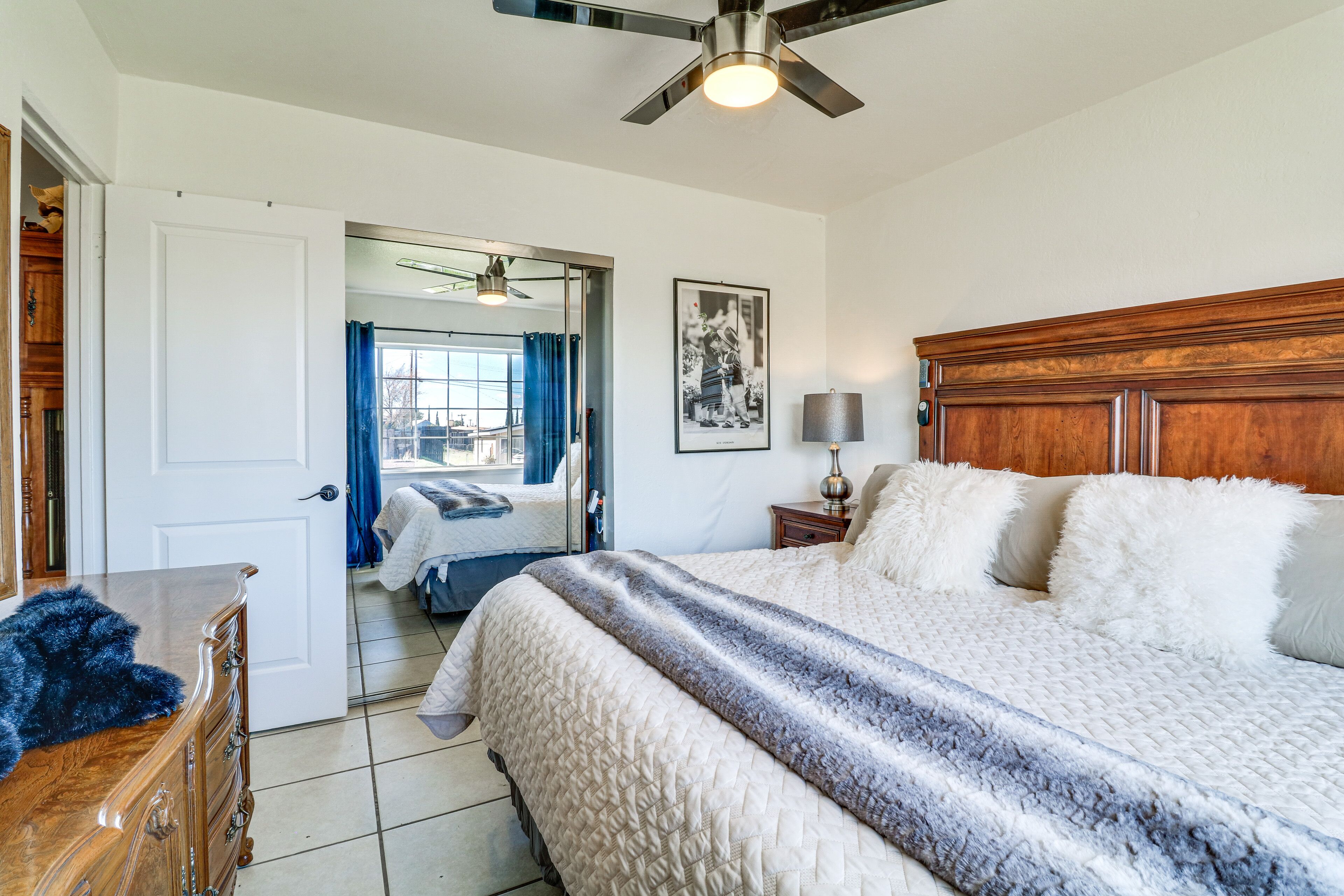 Une chambre à coucher avec un grand lit, une tête de lit en bois, un ventilateur de plafond, une table de chevet avec une lampe et une commode.