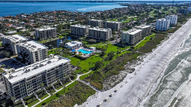 An aerial view of a coastal residential area with multiple high-rise buildings, a central swimming pool, and a beach. - Premier Beach View 2 Bedroom Condo (Longboat Key)