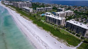 An aerial view of a coastal area with a beach, several high-rise buildings, and a clear view of the ocean. - Premier Beach View 2 Bedroom Condo (Longboat Key)