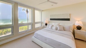 A bedroom with a large bed, two bedside tables, a ceiling fan, and a view of the ocean. - Premier Beach View 2 Bedroom Condo (Longboat Key)