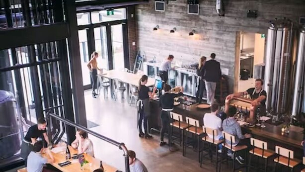 A spacious restaurant with high ceilings and large windows, featuring wooden tables and chairs, and a casual dining atmosphere. - NEW - Mountain Chic Escape - Whyte Ave - Netflix - Clean!
 (Edmonton)