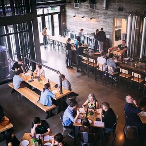 A spacious restaurant with high ceilings and large windows, featuring wooden tables and chairs, and a casual dining atmosphere. - NEW - Mountain Chic Escape - Whyte Ave - Netflix - Clean!
 (Edmonton)