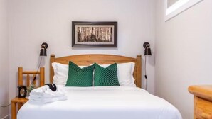 A neatly made bed with white and green pillows, a wooden headboard, and a framed picture on the wall. - NEW - Mountain Chic Escape - Whyte Ave - Netflix - Clean!
 (Edmonton)