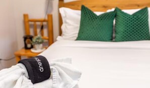 A neatly made bed with white bedding and a green pillow, a wooden chair, and a small table with a plant and a coffee maker. - NEW - Mountain Chic Escape - Whyte Ave - Netflix - Clean!
 (Edmonton)