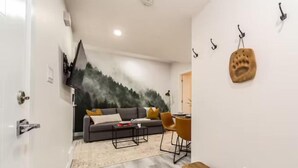 A modern living room with a grey sofa, a coffee table, and a dining area with a chair and table. - NEW - Mountain Chic Escape - Whyte Ave - Netflix - Clean!
 (Edmonton)