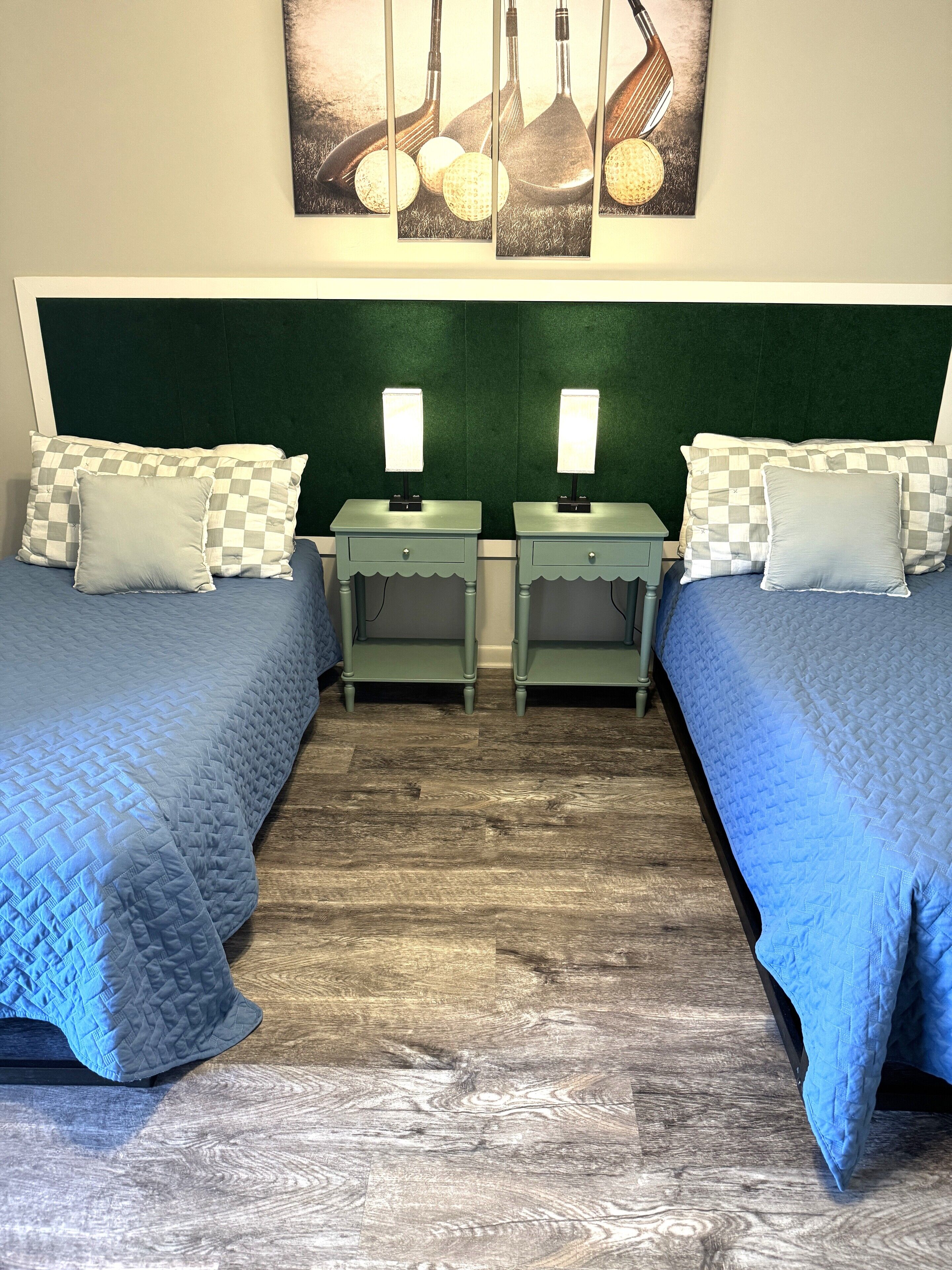 A room with two beds, each with a checkered pillow and a bedside table with a lamp.
