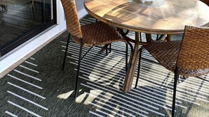 Un coin repas avec une table ronde en bois, des chaises en osier et une porte vitrée donnant sur un espace extérieur.