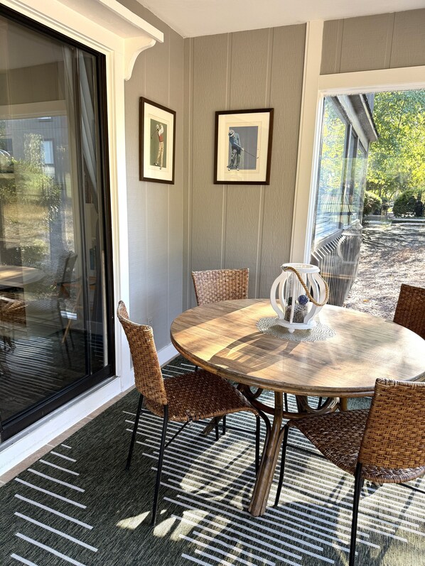 A dining area with a round wooden table, wicker chairs, and a glass door leading to an outdoor space.
