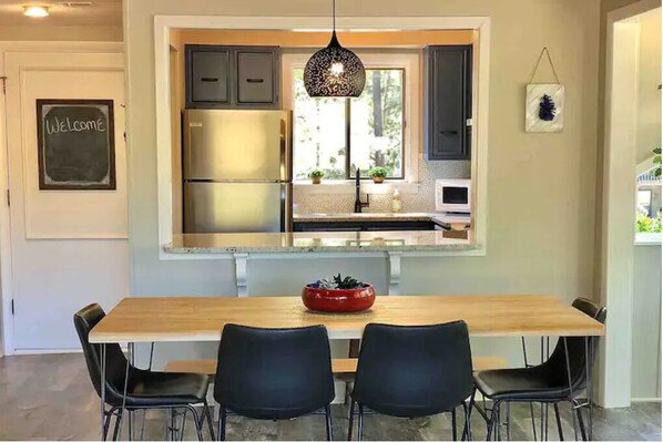 Une cuisine moderne dotée d’un îlot central intégré, d’appareils électroménagers en acier inoxydable et de chaises noires disposées autour d ’une table en bois.