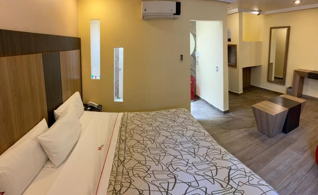Una camera d'albergo con un letto grande, comodini, un condizionatore d'aria, uno specchio e un piccolo angolo salotto.