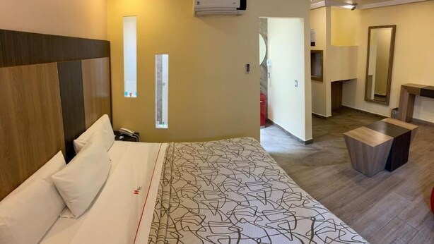 A hotel room with a large bed, bedside tables, an air conditioning unit, a mirror, and a small seating area. - HOTEL M RED (Mexico City)