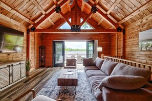 A log cabin interior with a wooden ceiling, a sofa, a coffee table, and a view through the open door.
