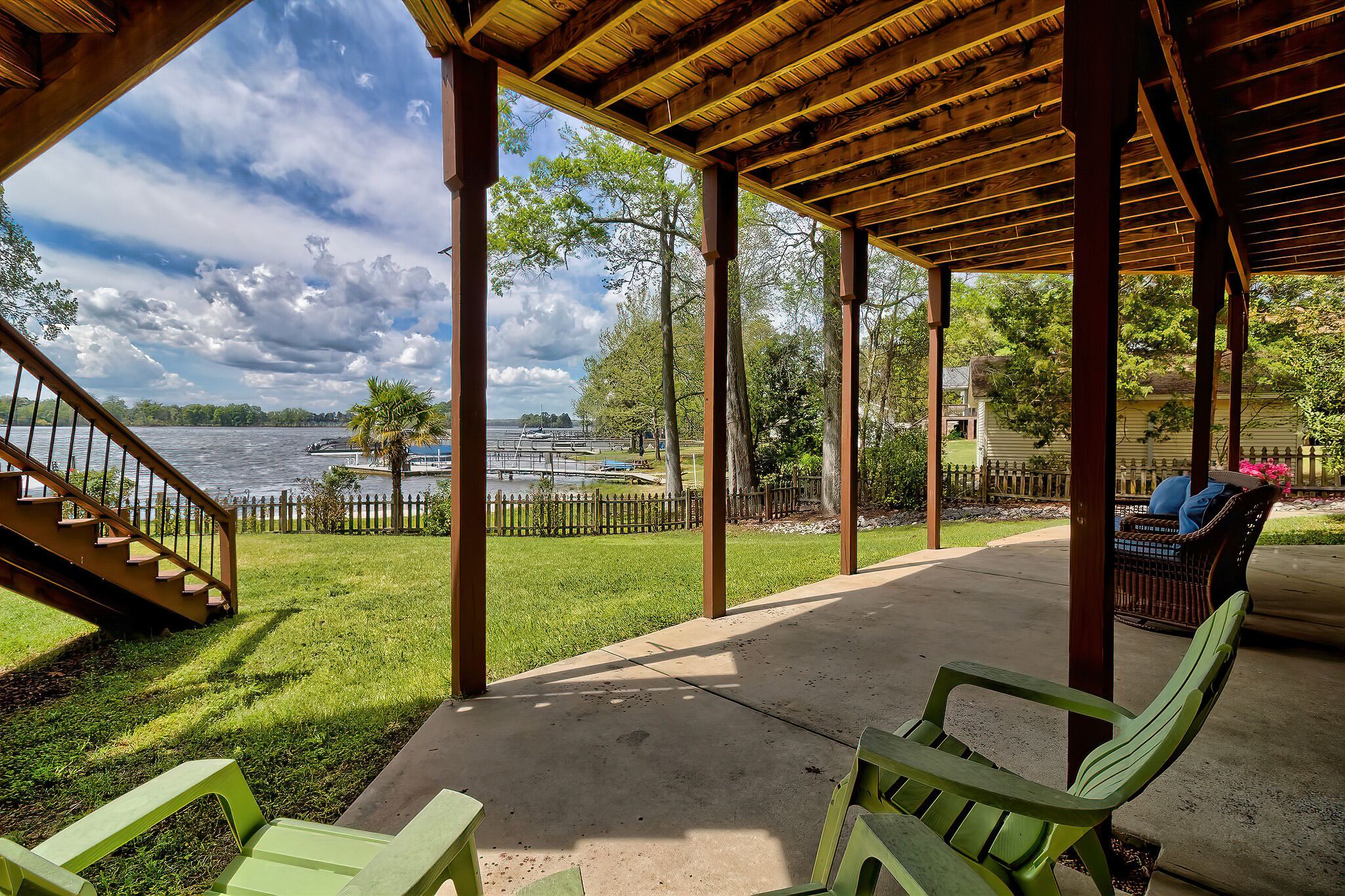 A covered outdoor area with a wooden deck, a concrete walkway, and a view of a lake with a dock and a boat.