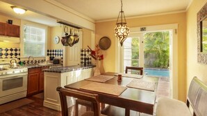 Une cuisine avec un coin repas, des meubles de rangement en bois, une cuisinière et un luminaire suspendu.
