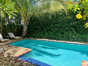Una piscina rettangolare con acqua cristallina, circondata da vegetazione lussureggiante e un bordo piastrellato.