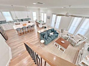 A spacious living area with a sofa, chairs, and a coffee table. There is a kitchen in the background with white cabinets and a dining area with a table and chairs.