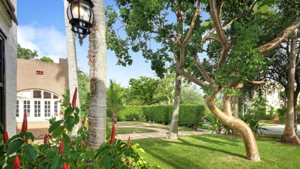 Un jardín cuidado con un sendero, palmeras y un edificio con un ventanal curvo.