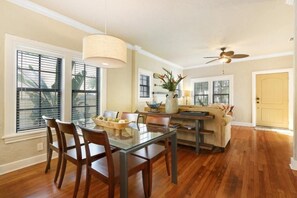 A dining area with a glass table, wooden chairs, and a ceiling fan.