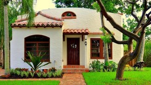 Una casa pequeña de una sola planta con fachada blanca, puerta marrón y tejado de tejas.
