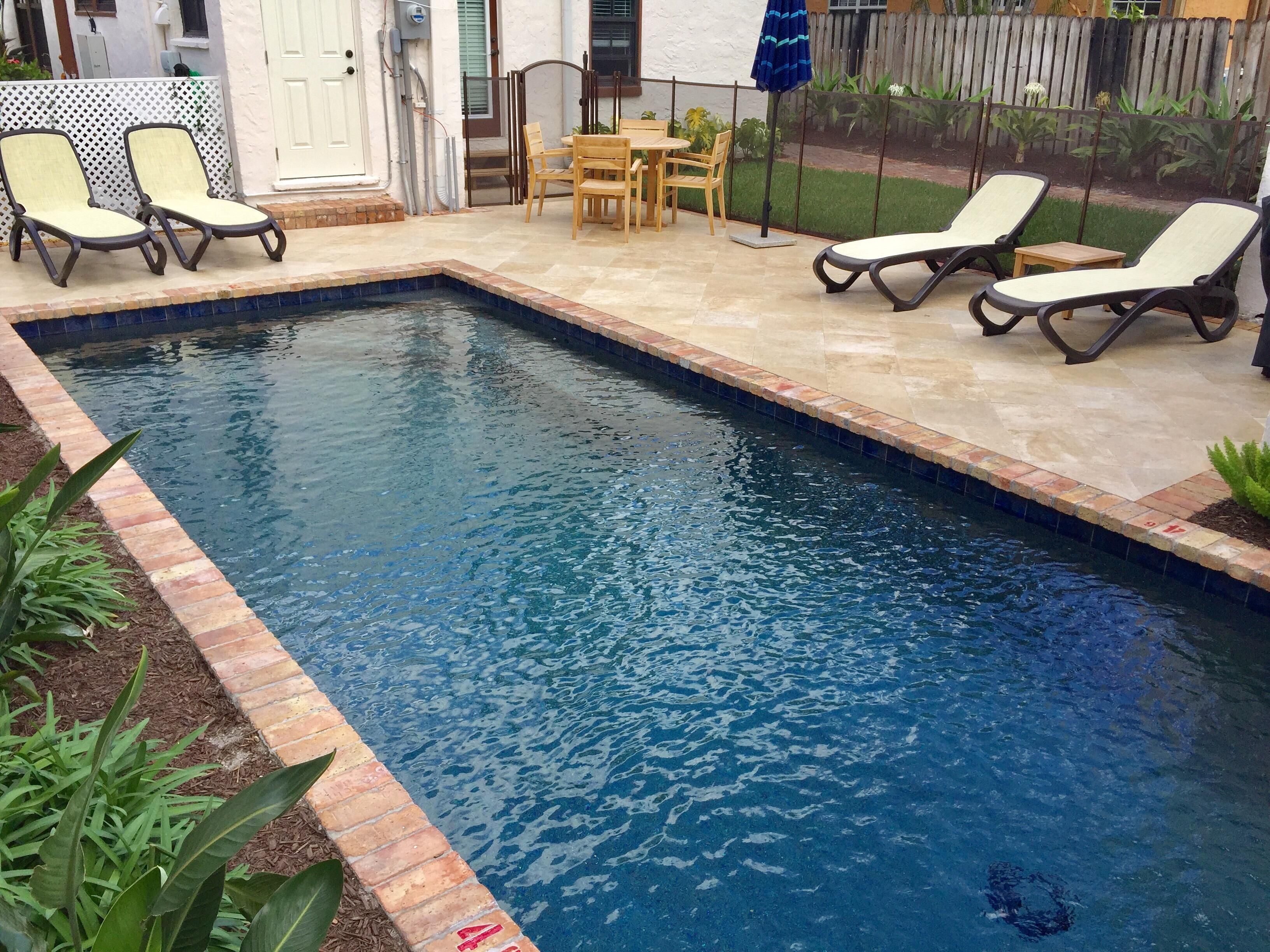 A rectangular swimming pool with a tiled border, surrounded by lounge chairs and a small table.