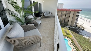 Ein Balkon mit einer Couch, Stühlen und einem kleinen Tisch mit Blick auf einen Strand und einen Poolbereich.