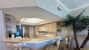 A kitchen with a central island, wooden chairs, a refrigerator, cabinets, and a potted plant. - 1303 is a beautiful 2br/2ba 13th floor unit with a magnificent view! (Panama City Beach)