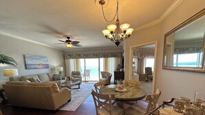 A spacious living room with a large sofa, a dining table with chairs, a ceiling fan, and a chandelier. - 1303 is a beautiful 2br/2ba 13th floor unit with a magnificent view! (Panama City Beach)