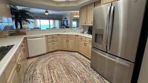 A modern kitchen with a large stainless steel refrigerator, wooden cabinets, and a patterned rug. - 1303 is a beautiful 2br/2ba 13th floor unit with a magnificent view! (Panama City Beach)