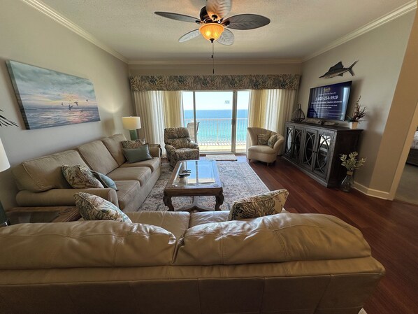 Una sala de estar con sofá, sillones, una mesa de centro, televisor y un balcón con vistas al océano.