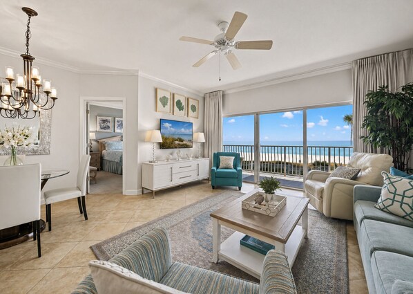 A spacious living room with a balcony overlooking the beach, a dining area, and a kitchen.