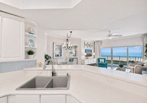 A modern kitchen with a double sink, a chandelier, and a view of the ocean.