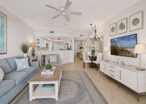 A spacious living room with a sofa, coffee table, and dining area with chairs and a chandelier.