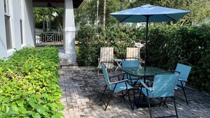 An outdoor patio with a table and chairs, surrounded by greenery and a white building. - Grey Mist Modern 3bd 2ba on Quiet Street (West Palm Beach)