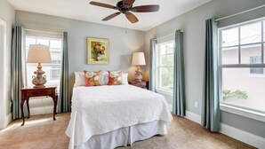 A bedroom with a large bed, two bedside tables with lamps, a ceiling fan, and a window with curtains. - Grey Mist Modern 3bd 2ba on Quiet Street (West Palm Beach)