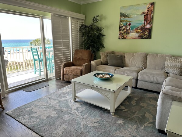 A living room with a beige sofa, a brown armchair, a glass coffee table with a bowl, a large potted plant, and a painting on the wall. - Coral Reef Unit #301Specious 4br right on the water for big family vacations! (Panama City Beach)