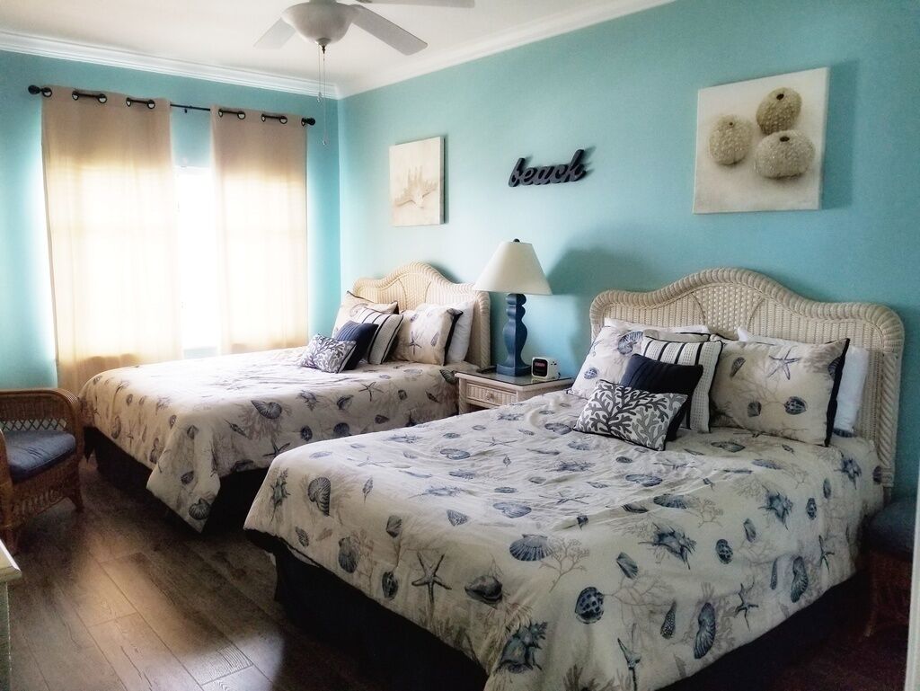 A room with two beds, each with a patterned bedspread, a nightstand with a lamp, and a chair.