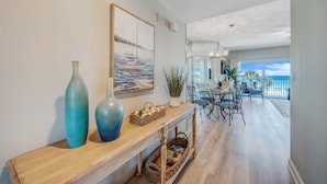 A modern living room with a wooden console table, a painting of a sailboat, and a view to the outside. - Beachfront 2br/2ba condo on the 3rd floor with free beach chairs included! (Panama City Beach)