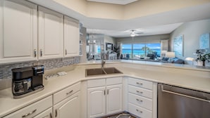 A modern kitchen with white cabinets, a built-in coffee maker, and a view to the living area. - Beachfront 2br/2ba condo on the 3rd floor with free beach chairs included! (Panama City Beach)