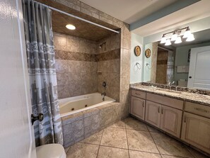 A bathroom with a bathtub, shower, vanity with a mirror, and a toilet.