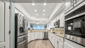 Cozinha moderna com eletrodomésticos de aço inoxidável, armários brancos e piso de madeira.